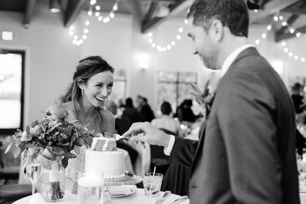 Black and white photo of couple sharing joyful moment while cutting wedding cake.