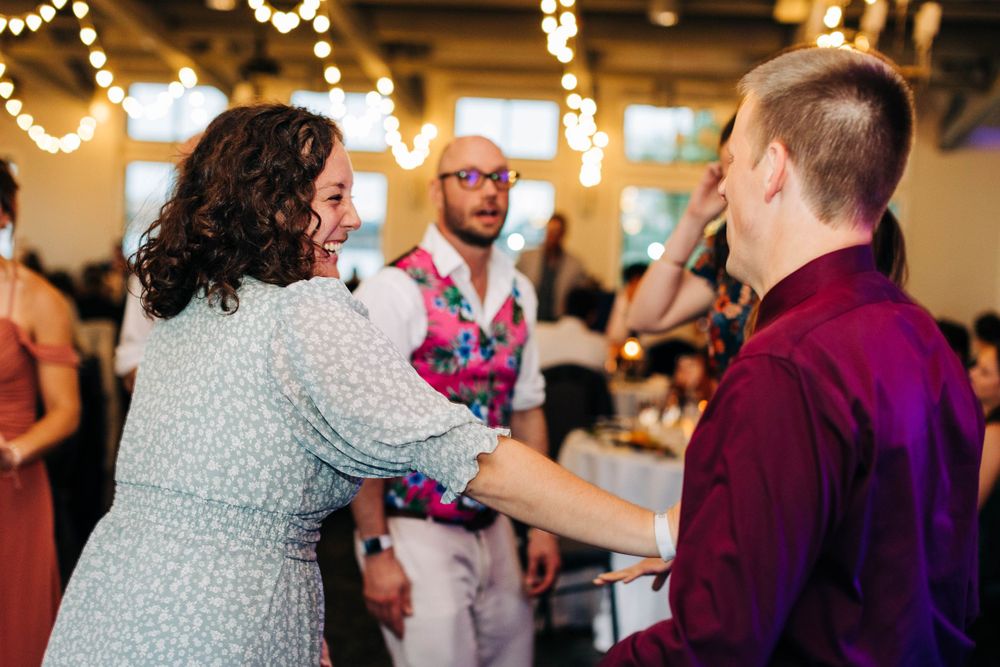 Wedding guests dancing and socializing under decorative string lights at reception.