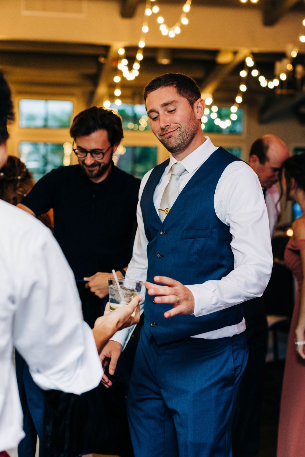 Man in blue vest socializes with guests at wedding reception.