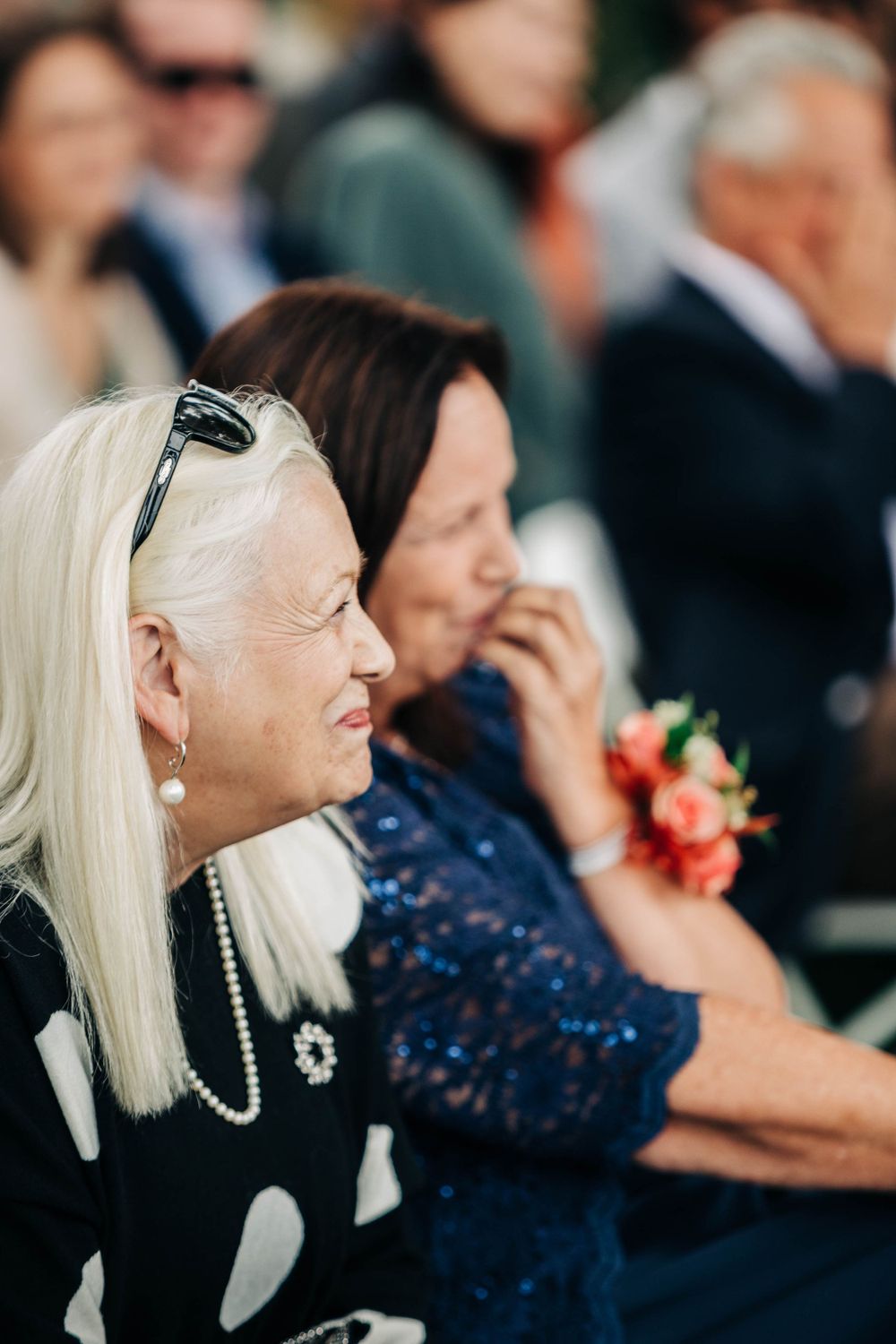 Wedding guests smile and laugh during an emotional outdoor ceremony moment.