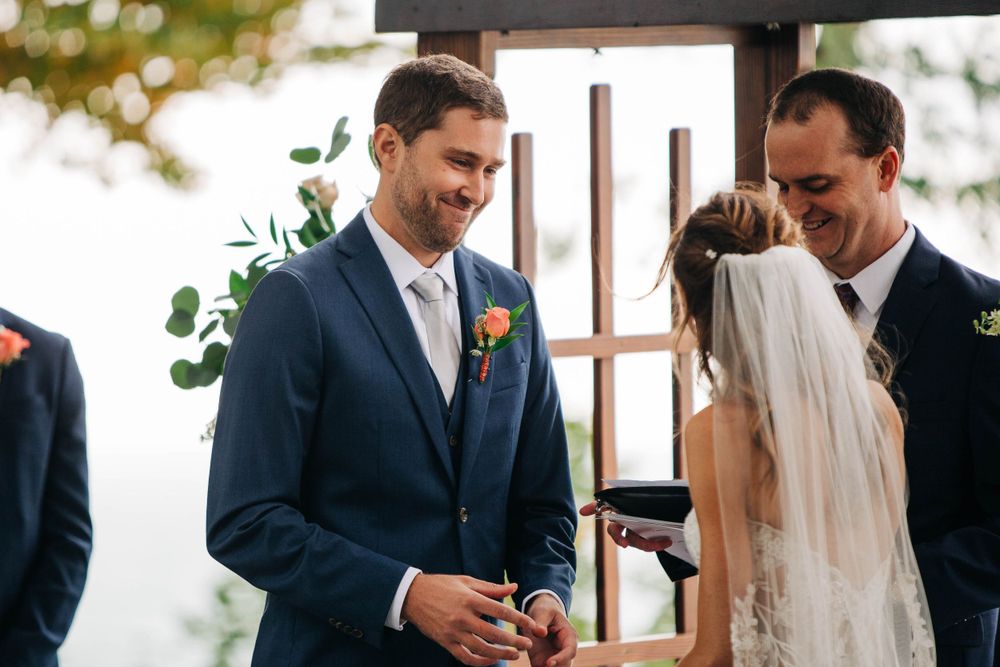A joyful moment during ring exchange at outdoor wedding ceremony under wooden archway.