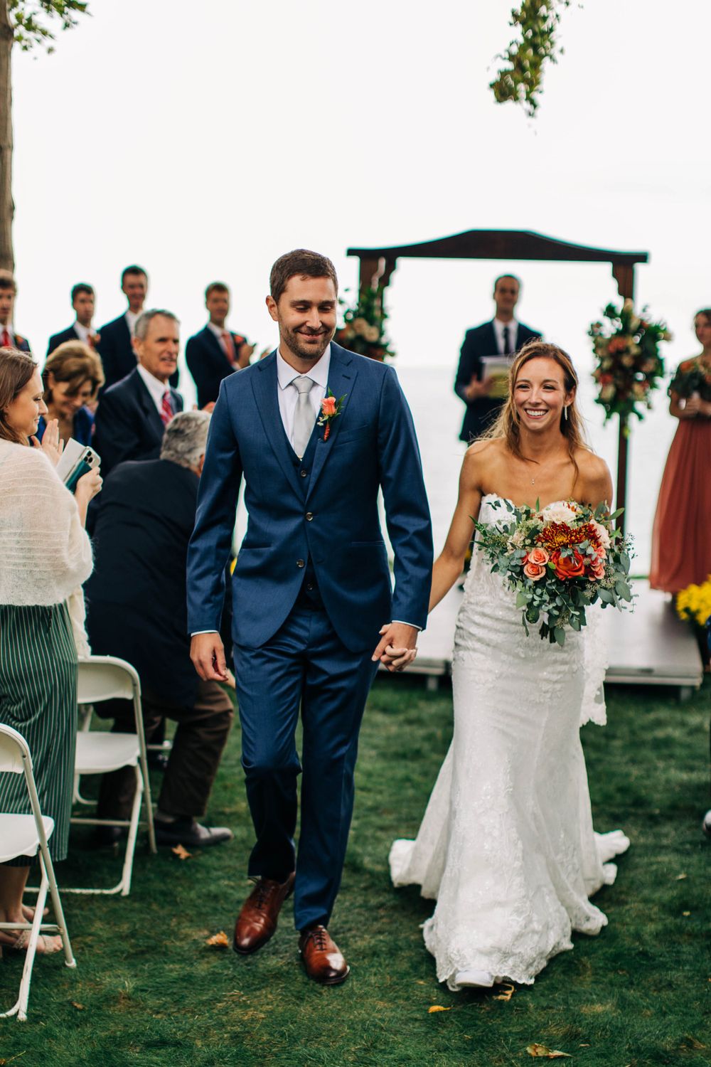 Newlyweds walk down the aisle together after outdoor ceremony with guest seating and decorative arch.