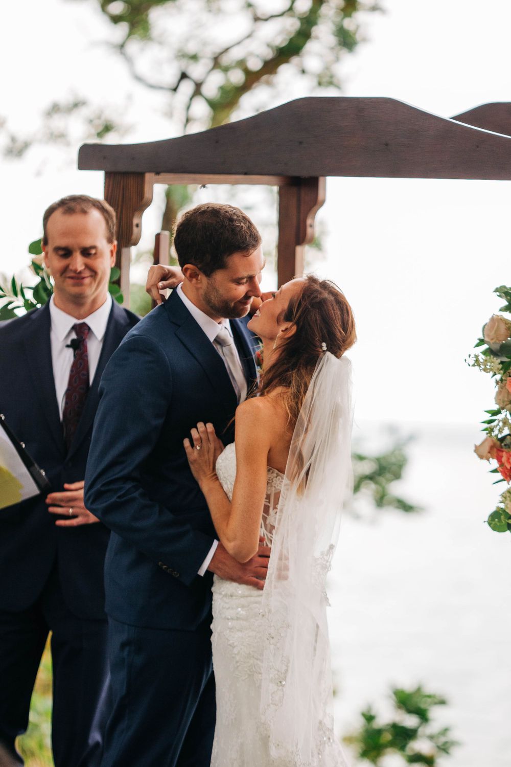 A couple shares their first kiss as newlyweds under a wooden ceremony arch.