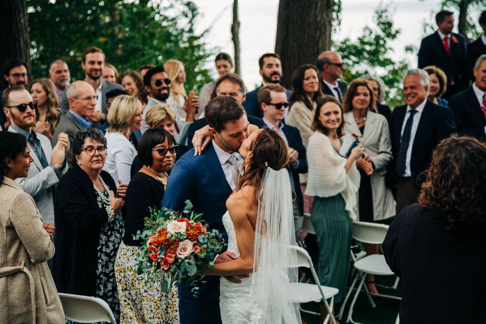 Wedding guests stand and cheer as the newlyweds kiss during their outdoor ceremony.