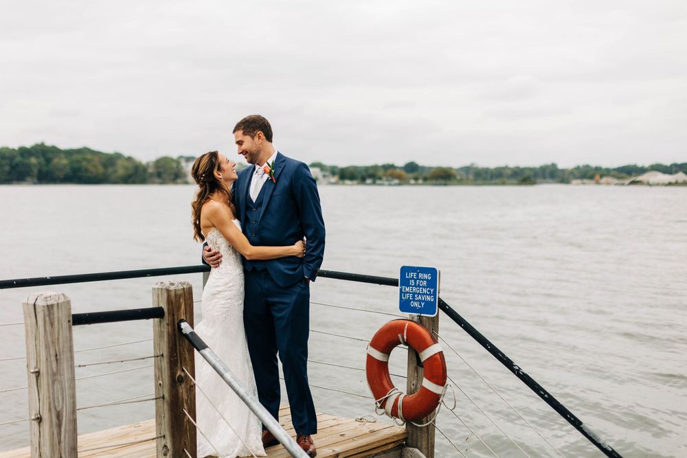 A couple shares a romantic moment on a dock with a life preserver in the background.