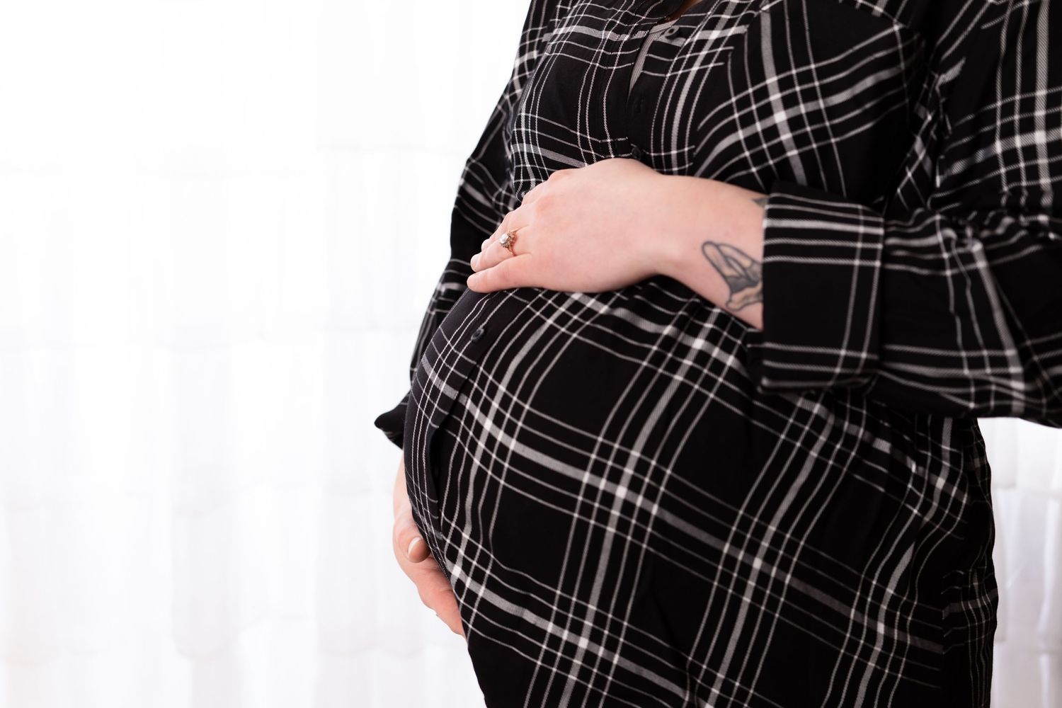 Close up of pregnant belly in black and white plaid maternity dress.