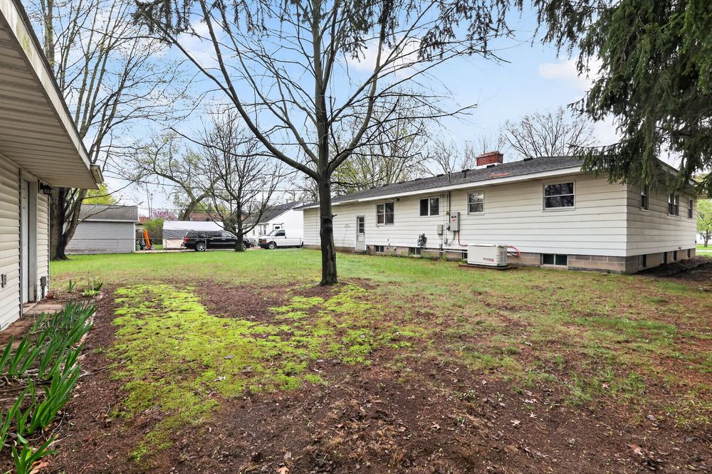 Ranch-style home exterior with large yard, mature trees, detached garage, and chimney.