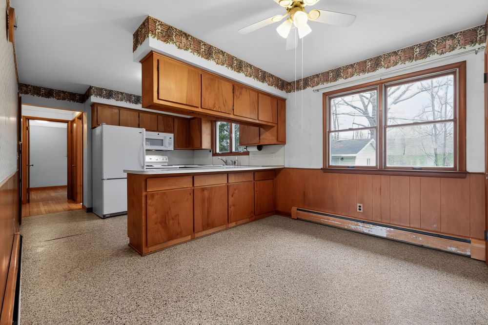 Kitchen with oak cabinets, stainless appliances, peninsula, baseboard heat, and decorative wallpaper border.