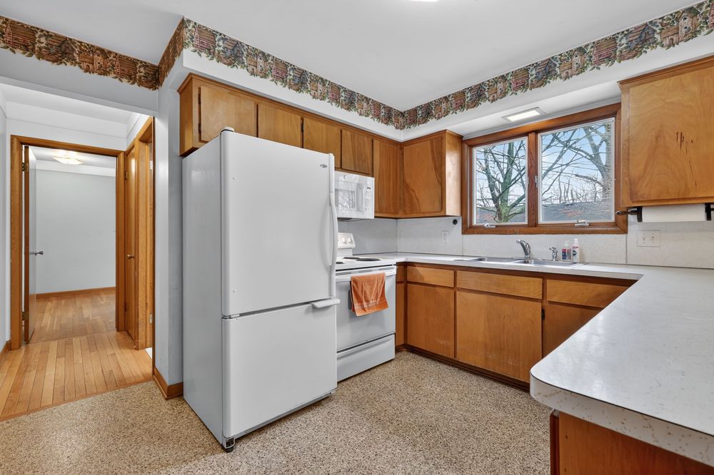 Kitchen with oak cabinets, white appliances, decorative border wallpaper, and window above the sink.