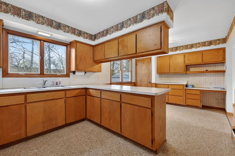 Spacious kitchen with oak cabinets, peninsula island, dual sinks, and decorative border wallpaper.