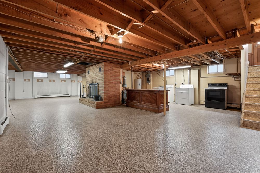 Spacious unfinished basement with epoxy floors, exposed wood beam ceiling, brick column, and wet bar area.