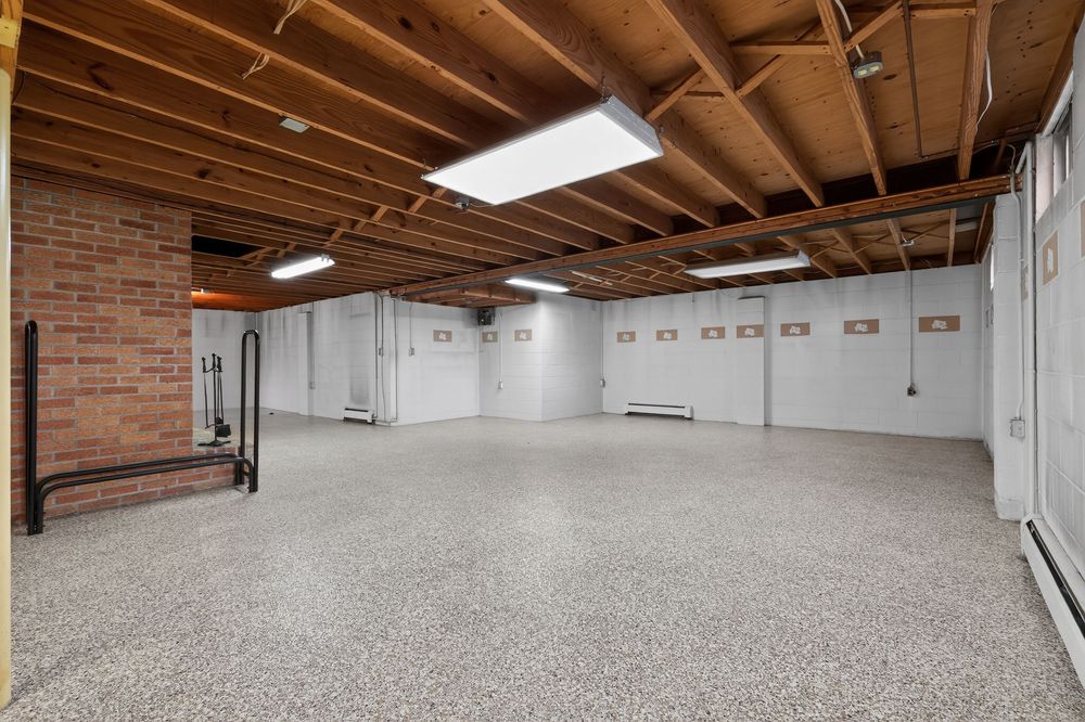 Large unfinished basement with epoxy speckled floors, exposed wood beam ceiling, brick wall, and baseboard heaters.