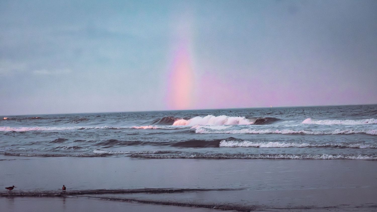 A rainbow falling onto the beach as waves crash ashore