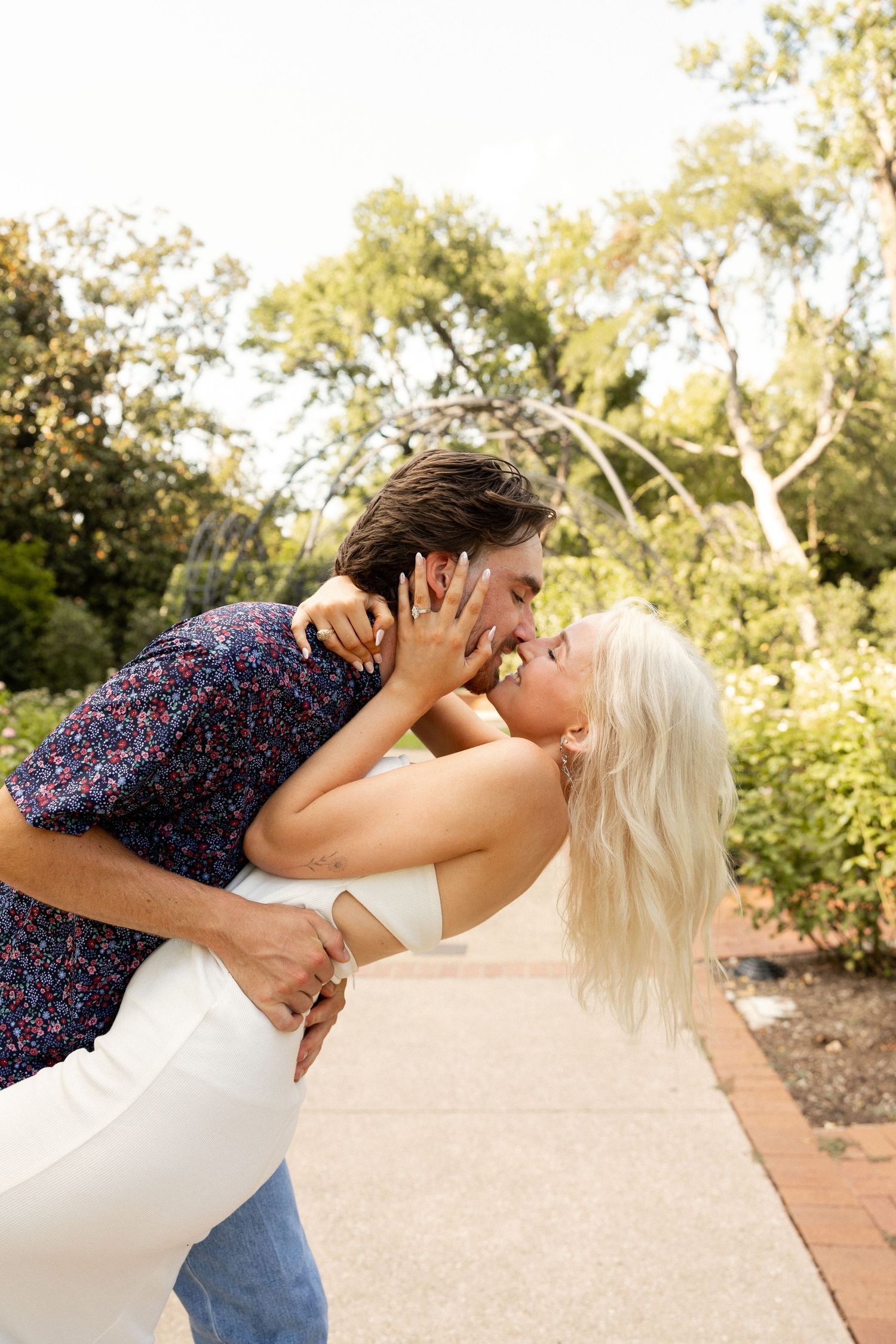 Romantic couple sharing playful moment on garden pathway during sunset photo session.