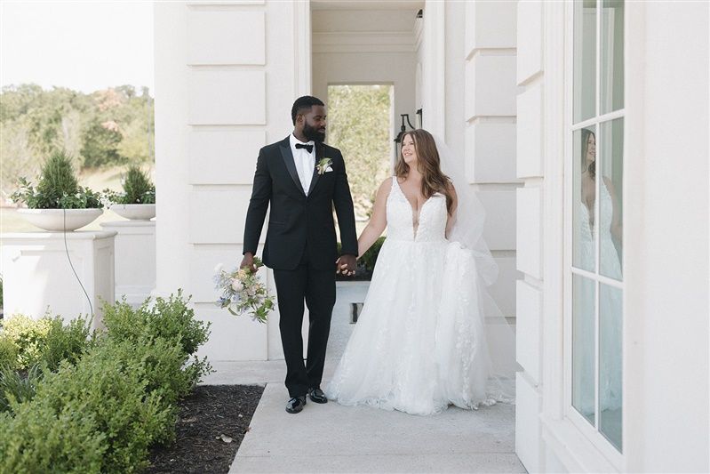 Newlywed couple walking together along a white pillared veranda.