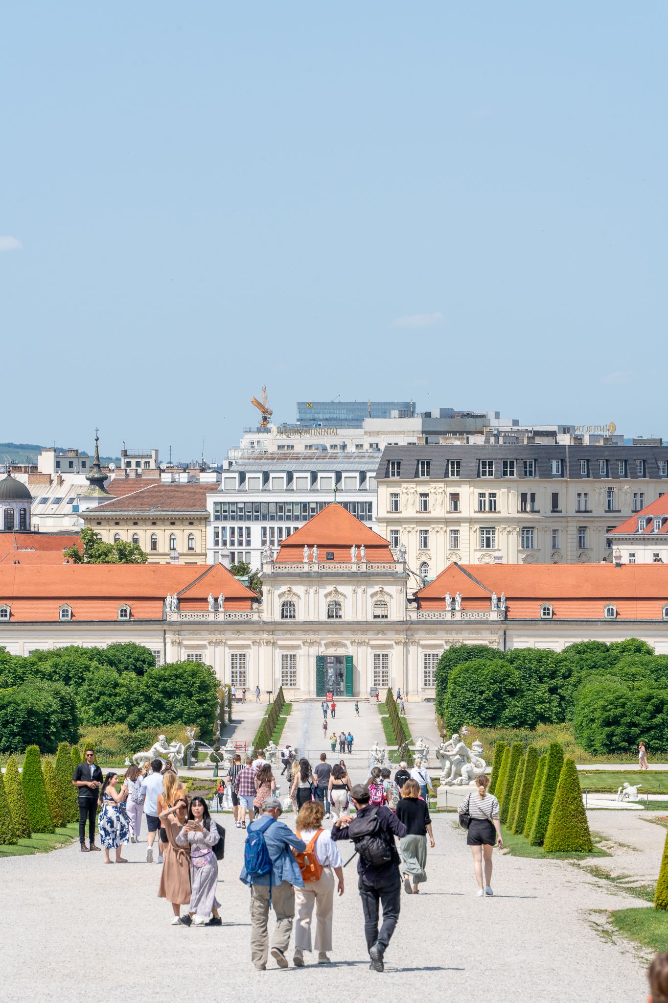 Visitors walking along the grand path towards Belvedere Palace in Vienna on a sunny summer day.