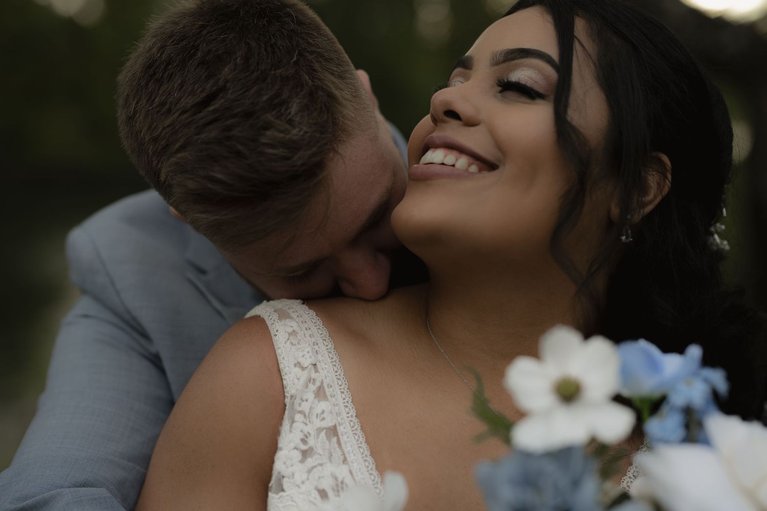 A joyful wedding moment captured in soft natural lighting with white floral details.