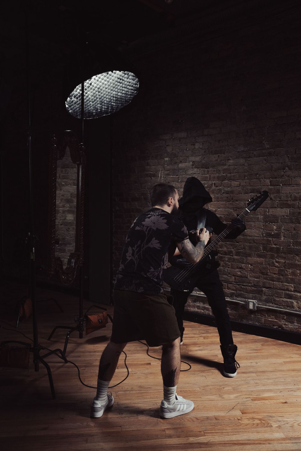 Dramatic photoshoot scene with studio lighting and brick wall background.