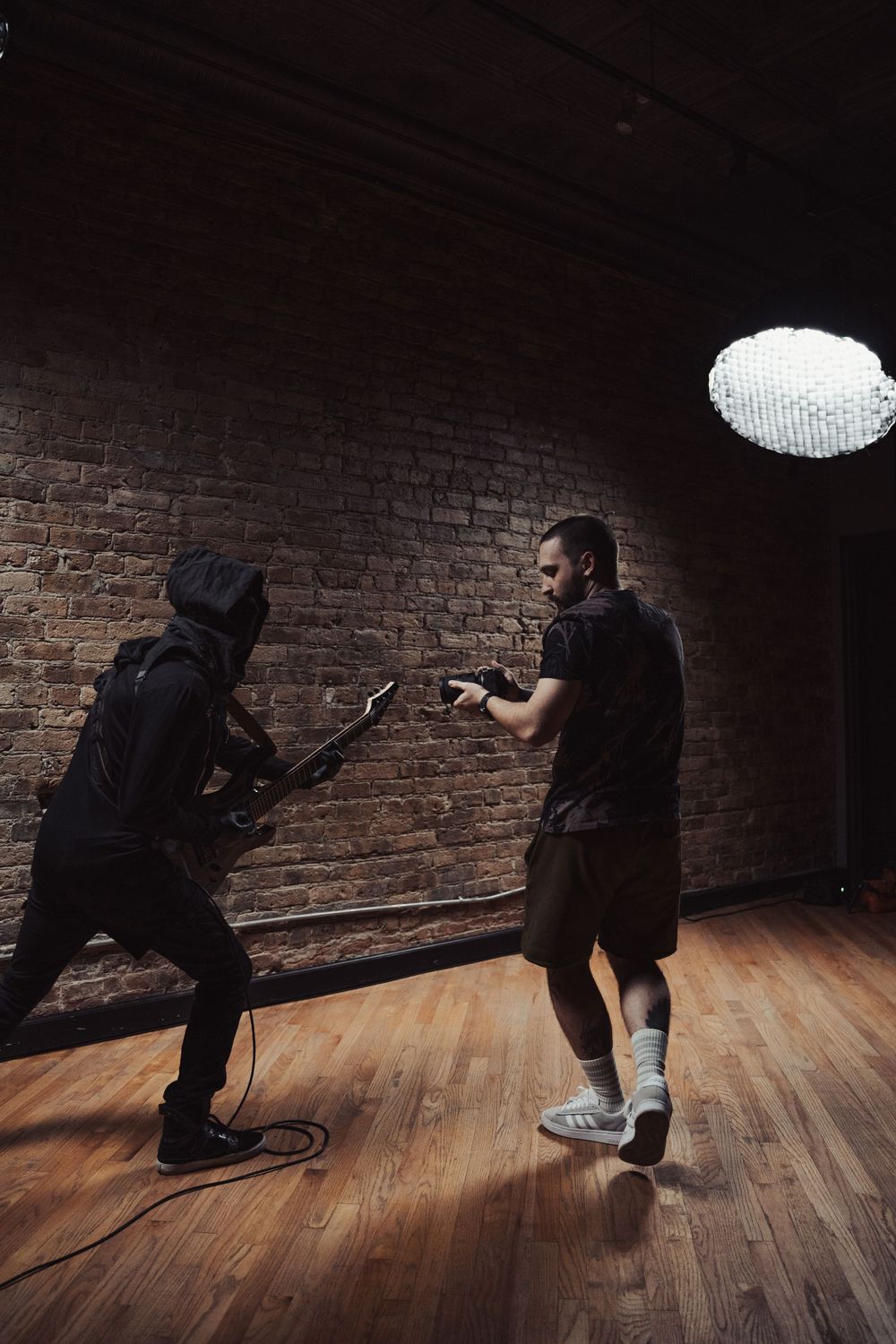 Two people performing dynamic poses under dramatic studio lighting against brick wall.