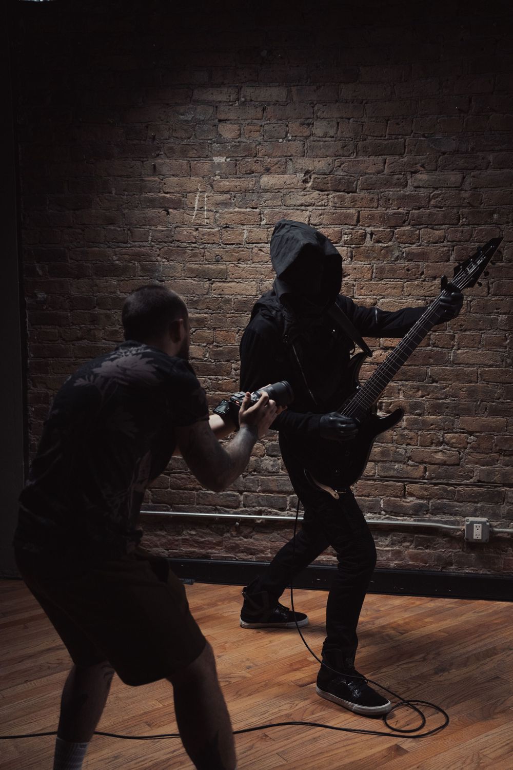 Dynamic photo shoot with dramatic poses against textured brick wall in dark studio.