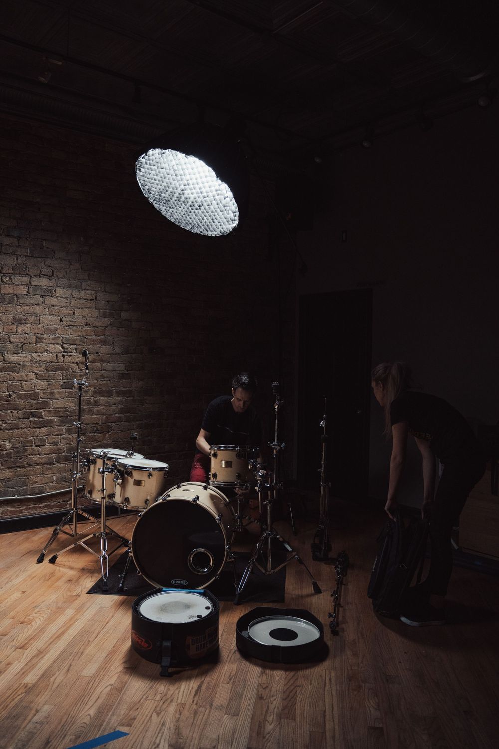Music studio setup with drum kit and lighting equipment on wooden floor against brick wall.