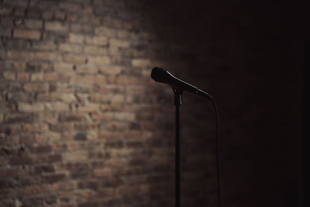 Microphone stand silhouetted against a dark brick wall in studio lighting.
