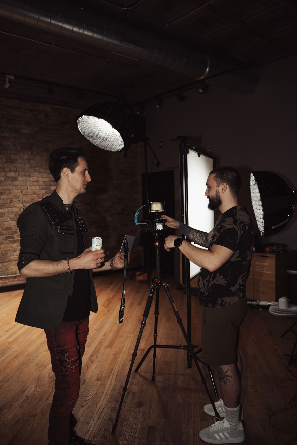 Two people discussing production details in a studio with overhead lighting and camera equipment.