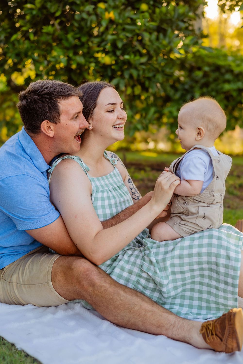 A family shares tender moments together on a white blanket outdoors during golden hour.