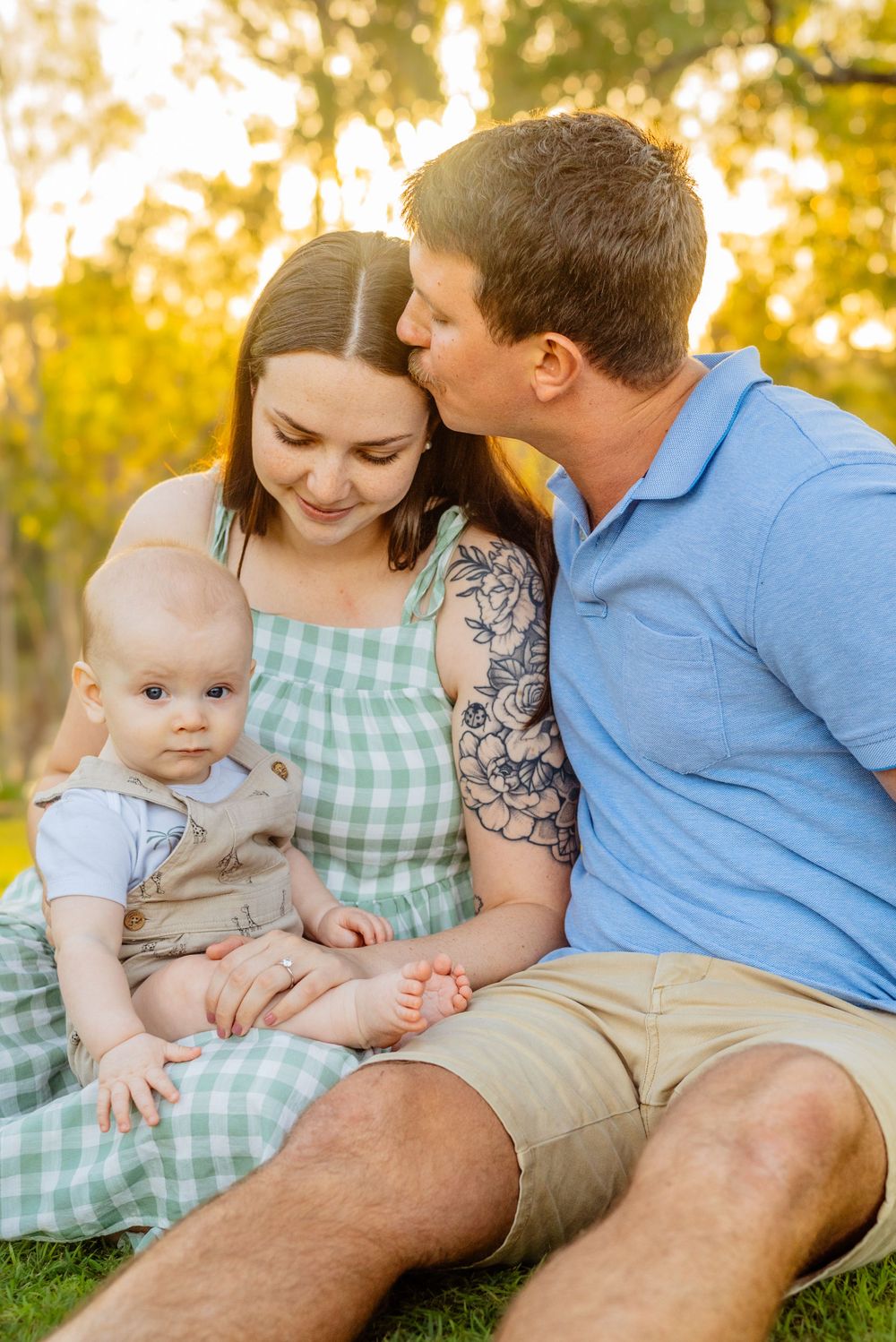 A family shares loving moments while sitting on grass during golden hour.