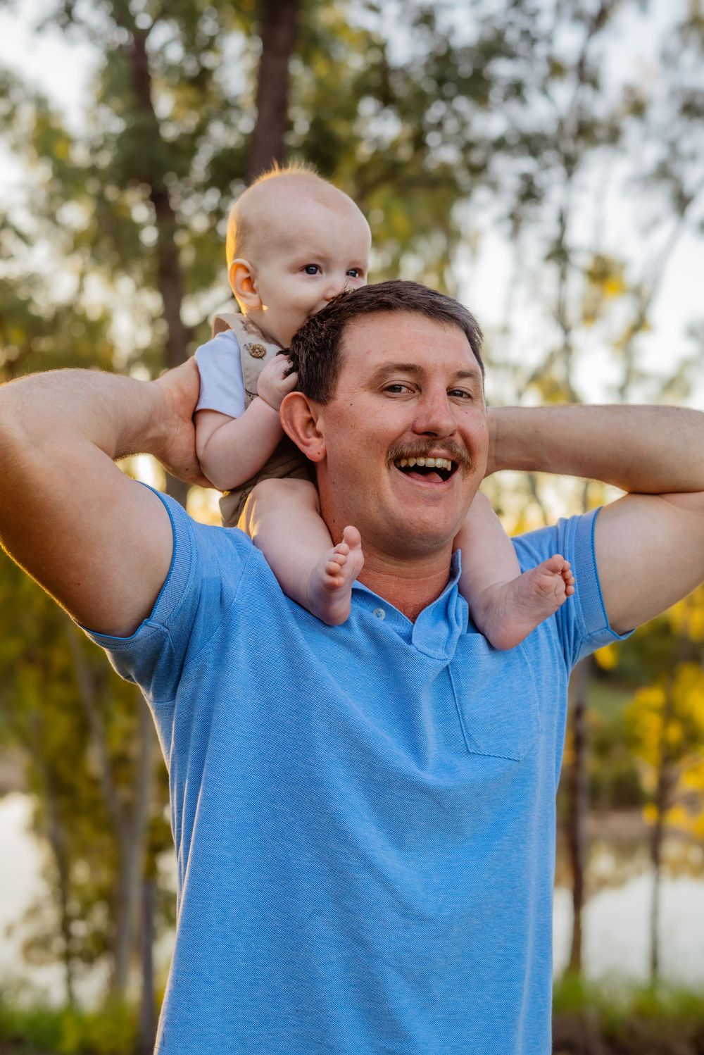 A baby rides on shoulders during a playful outdoor moment at sunset.