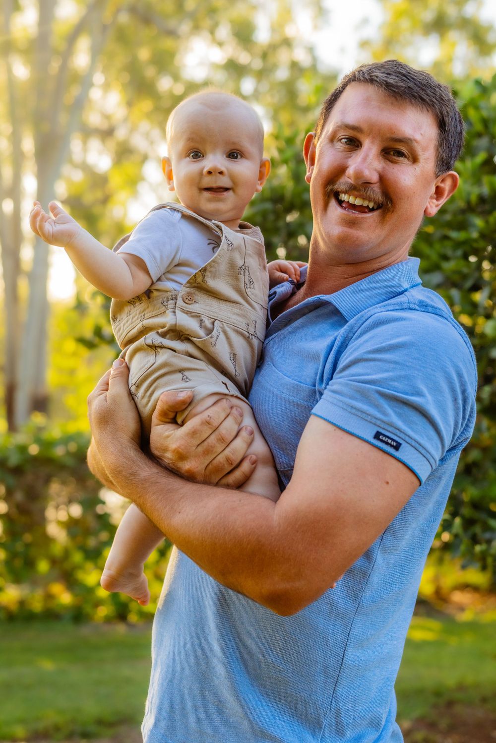 A cheerful outdoor portrait with a baby in tan overalls during golden hour.
