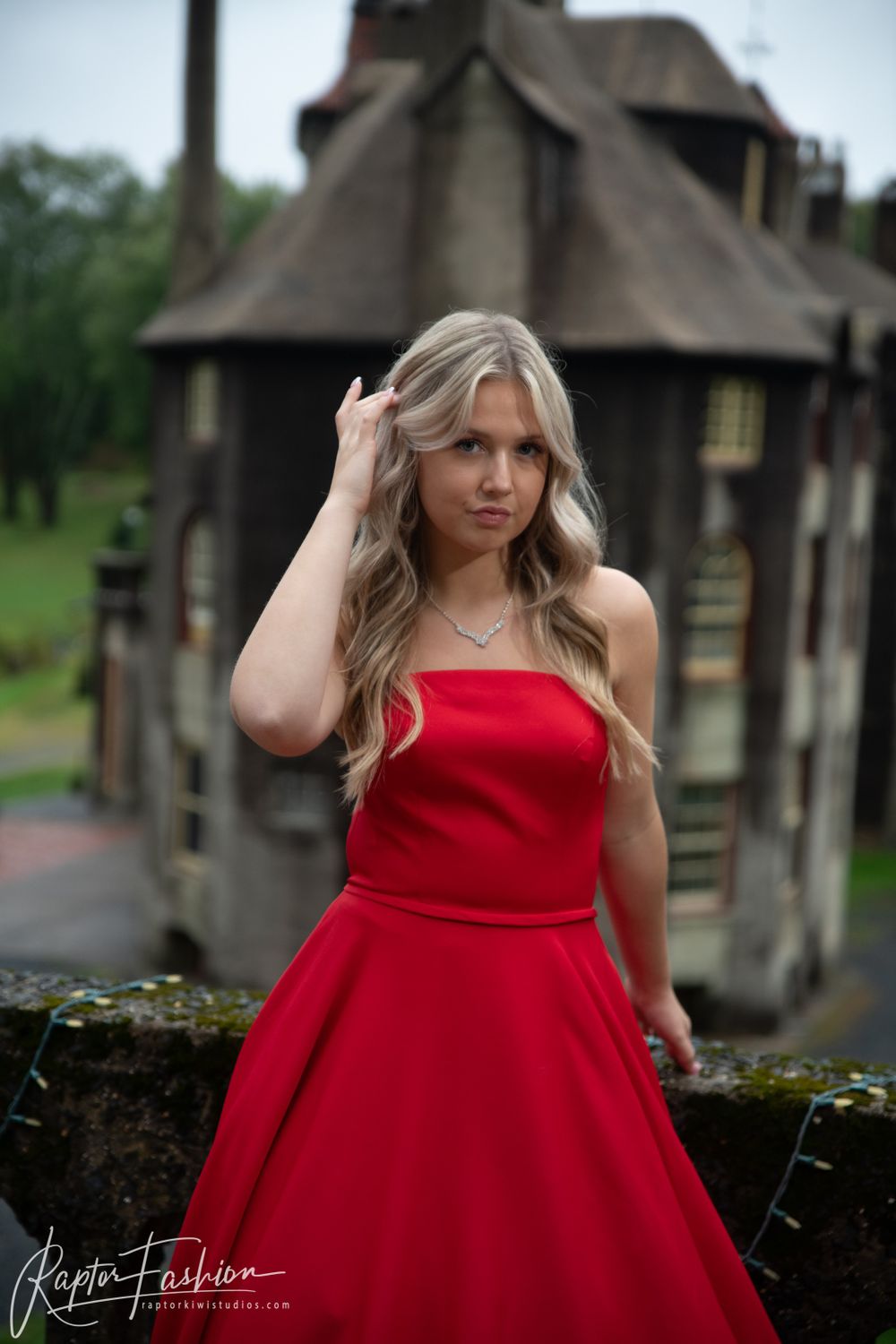 Elegant red formal dress photographed against gothic architecture backdrop in moody lighting.