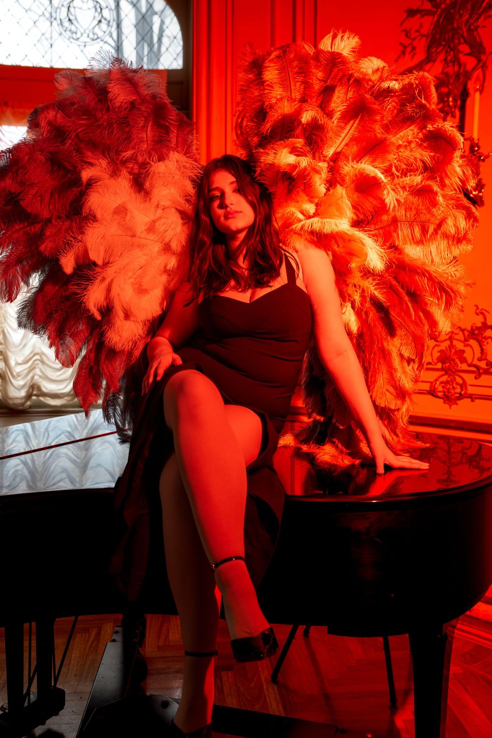 Moody red-lit scene with large feathered wings against piano and window backdrop.