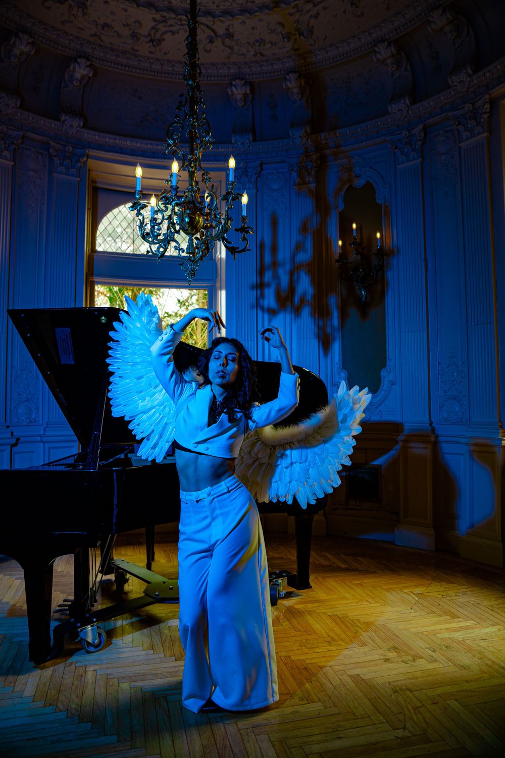 Dramatic blue-lit dance performance with angel wings next to grand piano.