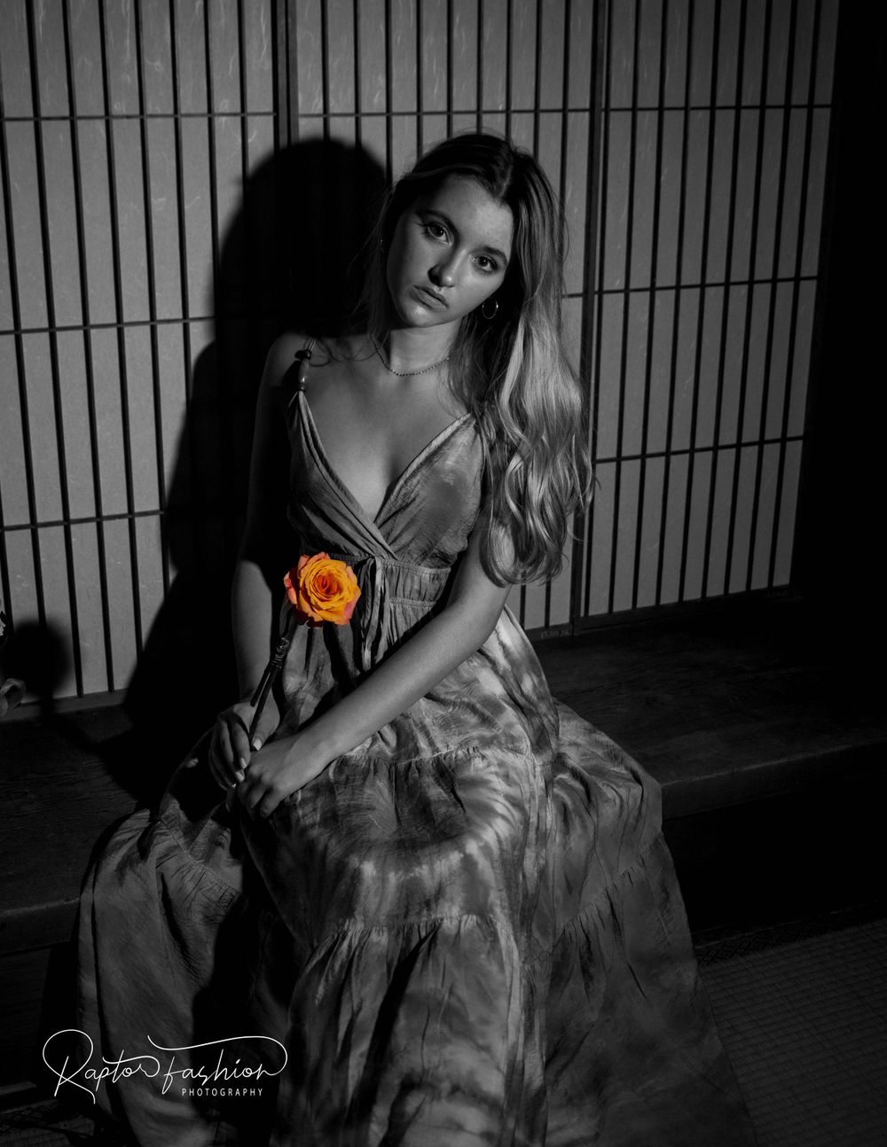 Black and white portrait with single orange flower accent against geometric background.