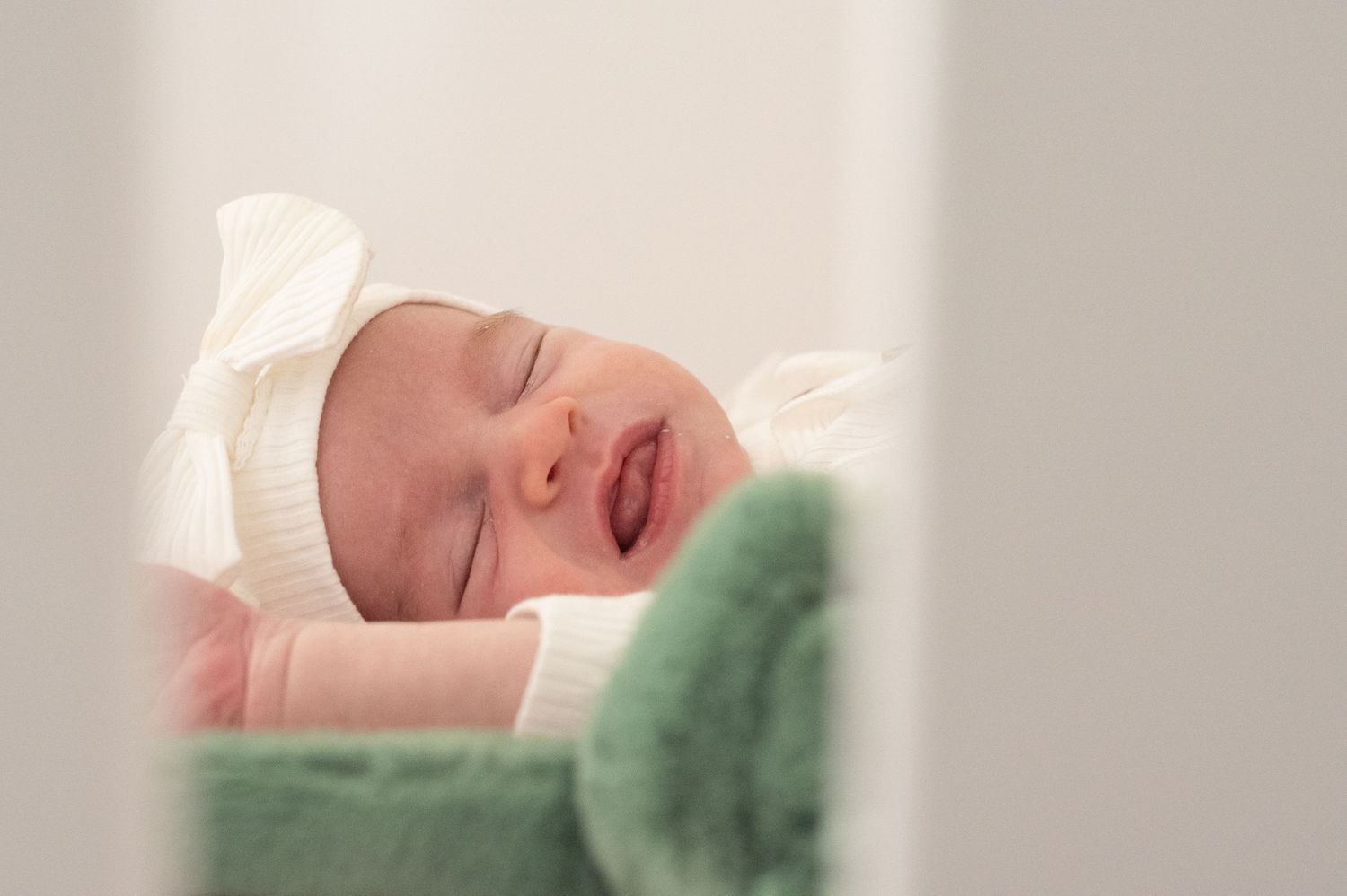 A baby in a cream-colored outfit looks at the camera while being held by parents outdoors.