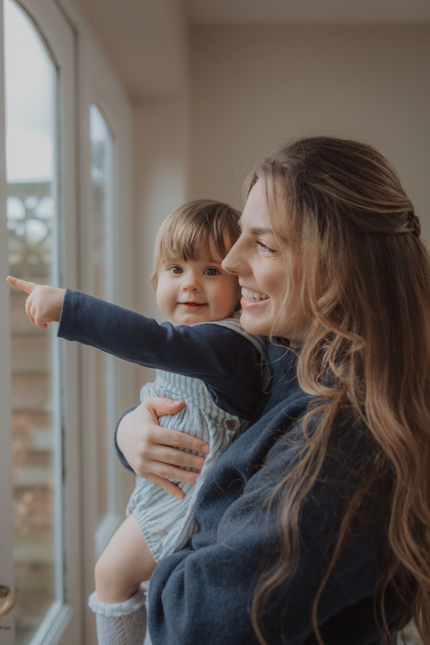 Parent and child share loving moment while looking out bright window together.