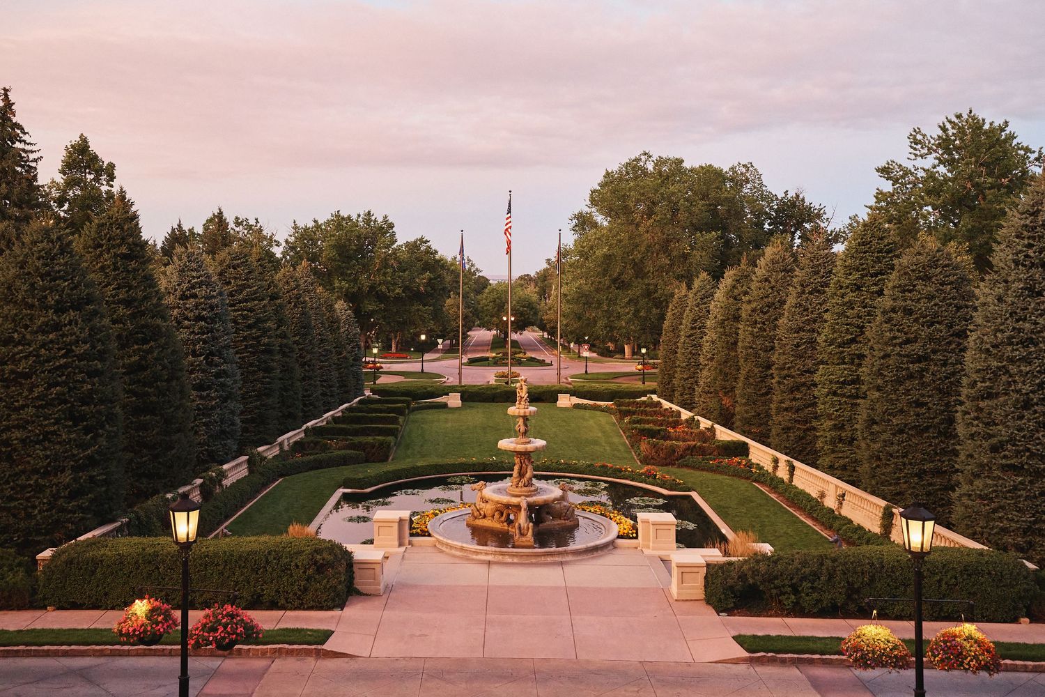 Symmetrical landscaped garden path with evergreen trees and benches at sunset.