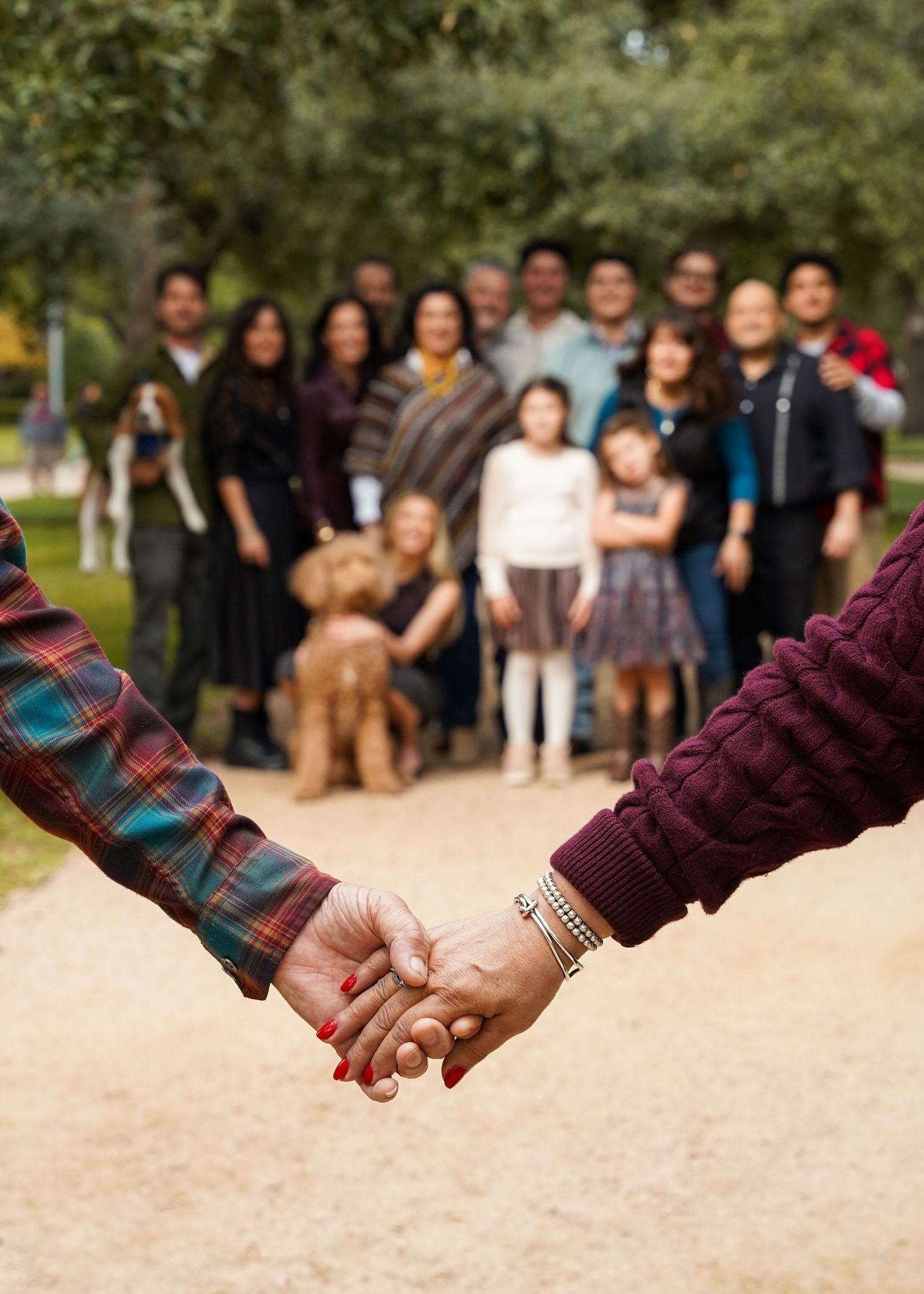 Two hands clasped together in foreground with group gathering visible behind.