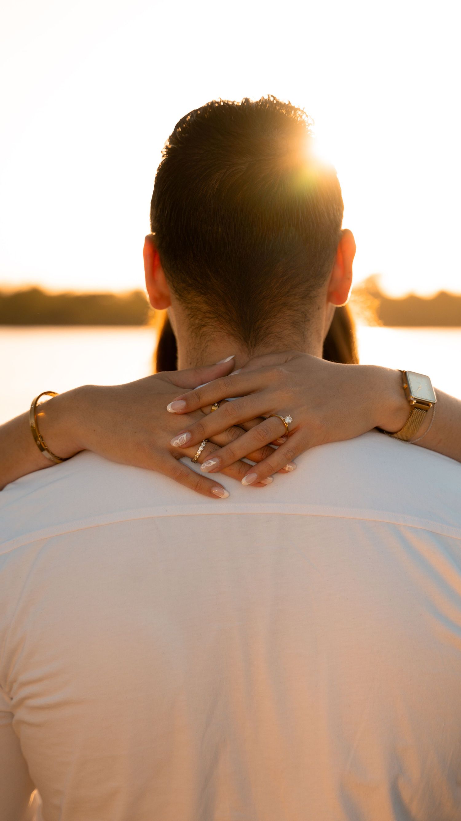 Two people reach out to hold hands across a blurred background during sunset.