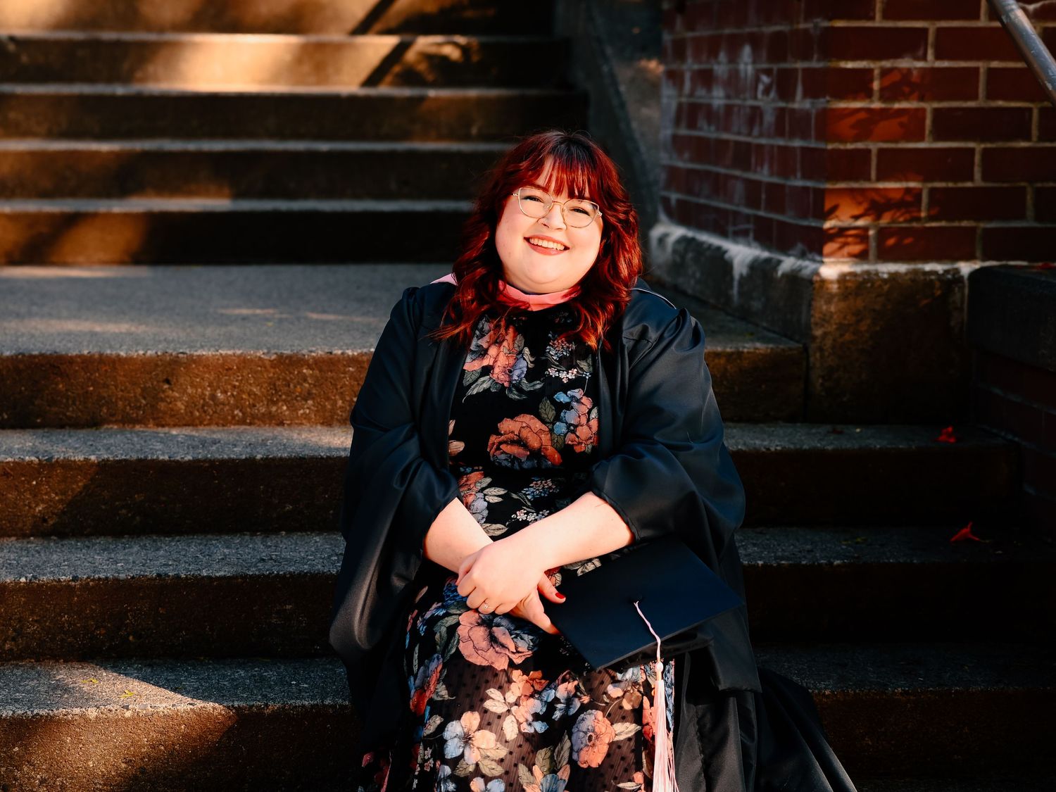 A floral dress and black cardigan outfit showcased on stone steps against a brick wall background.