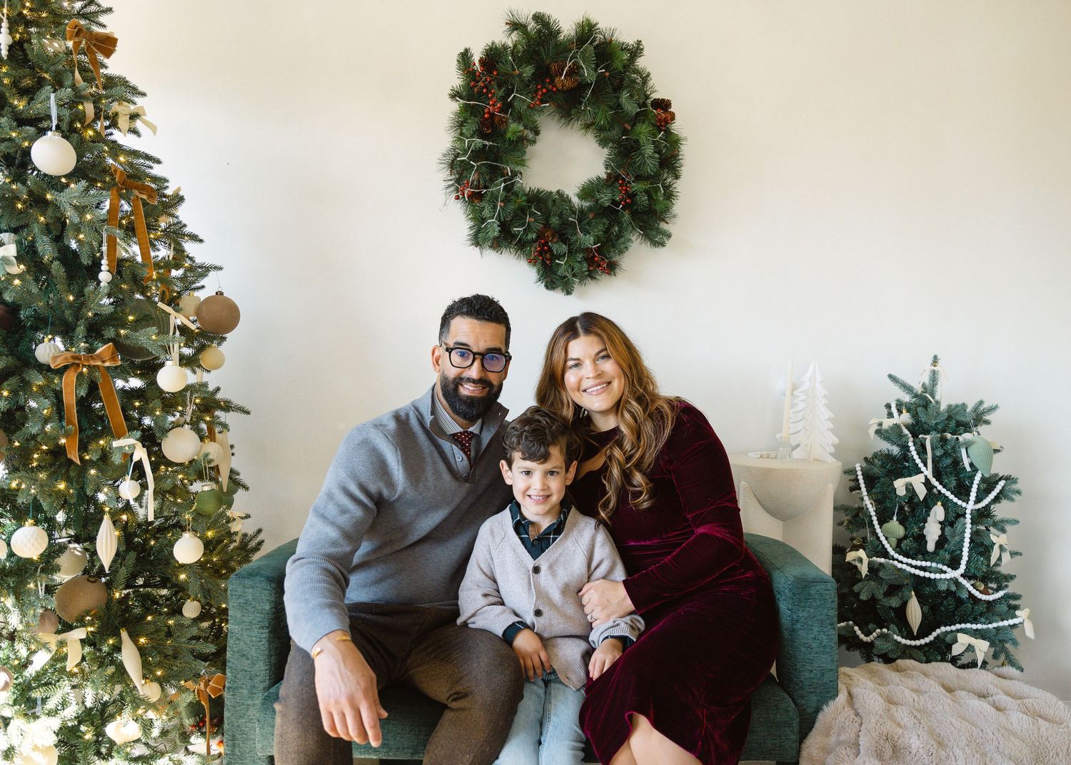 Two children in matching green velvet outfits pose together in front of decorated Christmas tree.