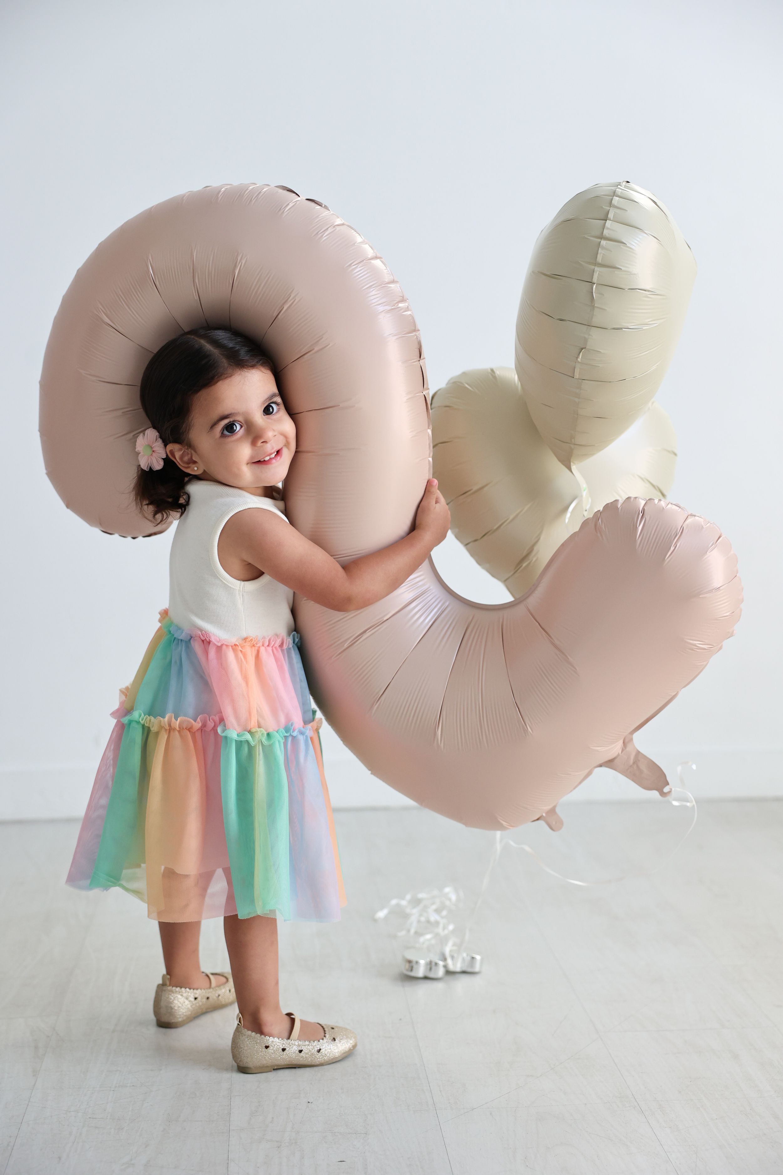 Young child hugging large blush pink balloon sculpture against white background.