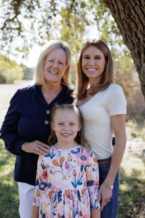 Three generations of family members smile together under a tree in natural lighting.