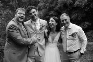 A joyous black and white candid wedding moment with the bridal party laughing together outdoors.