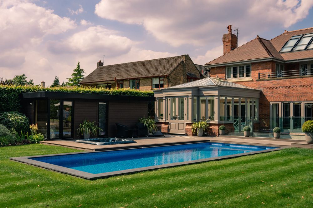 Modern luxury home with glass conservatory and rectangular swimming pool in manicured backyard.