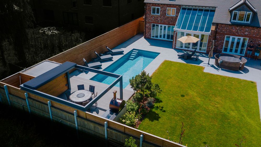 Aerial view of a modern backyard with rectangular swimming pool, lounge area and green lawn.