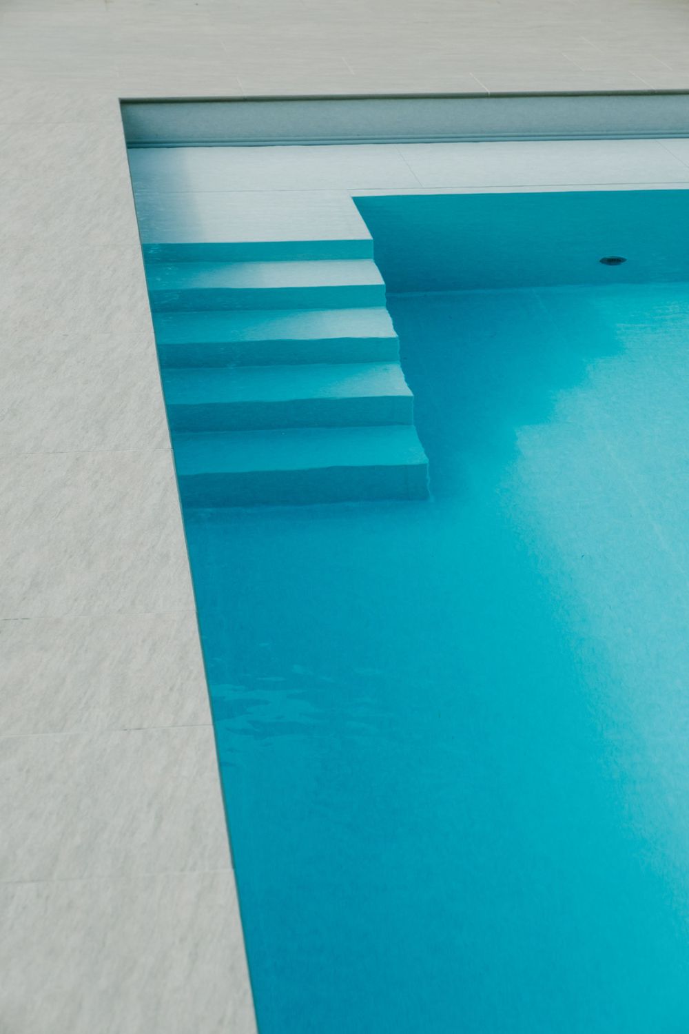 Minimalist swimming pool steps in white and turquoise blue creating geometric shapes.