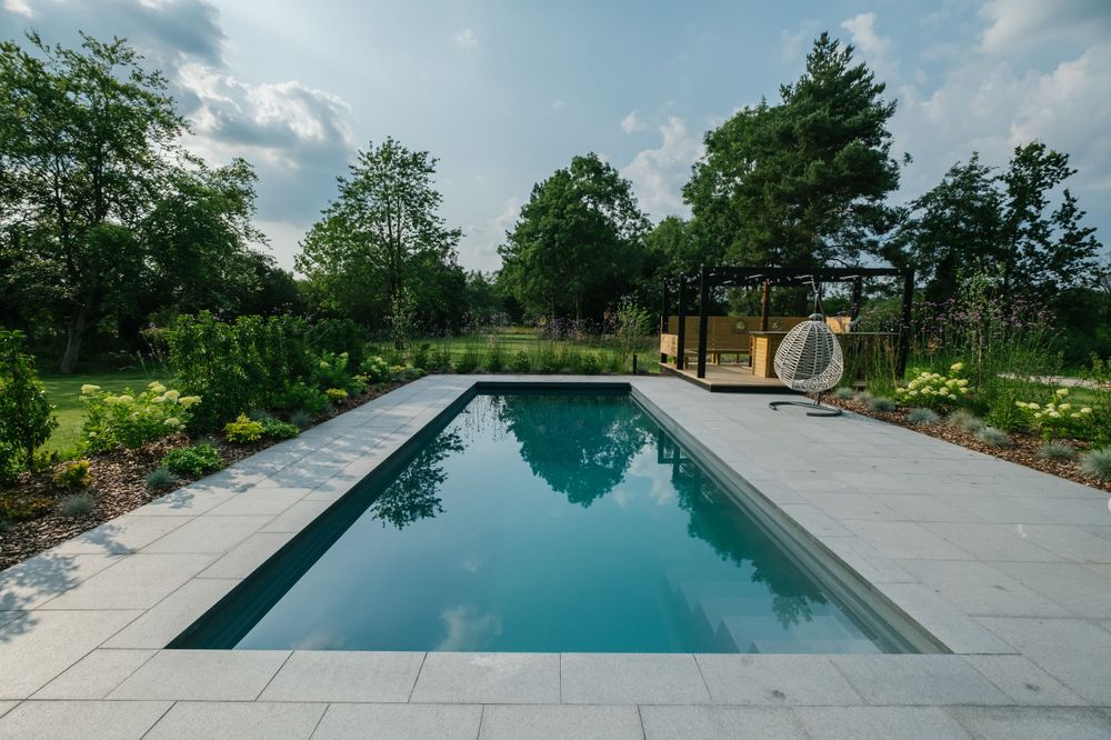 Rectangular swimming pool with stone paving surrounded by natural garden landscaping.