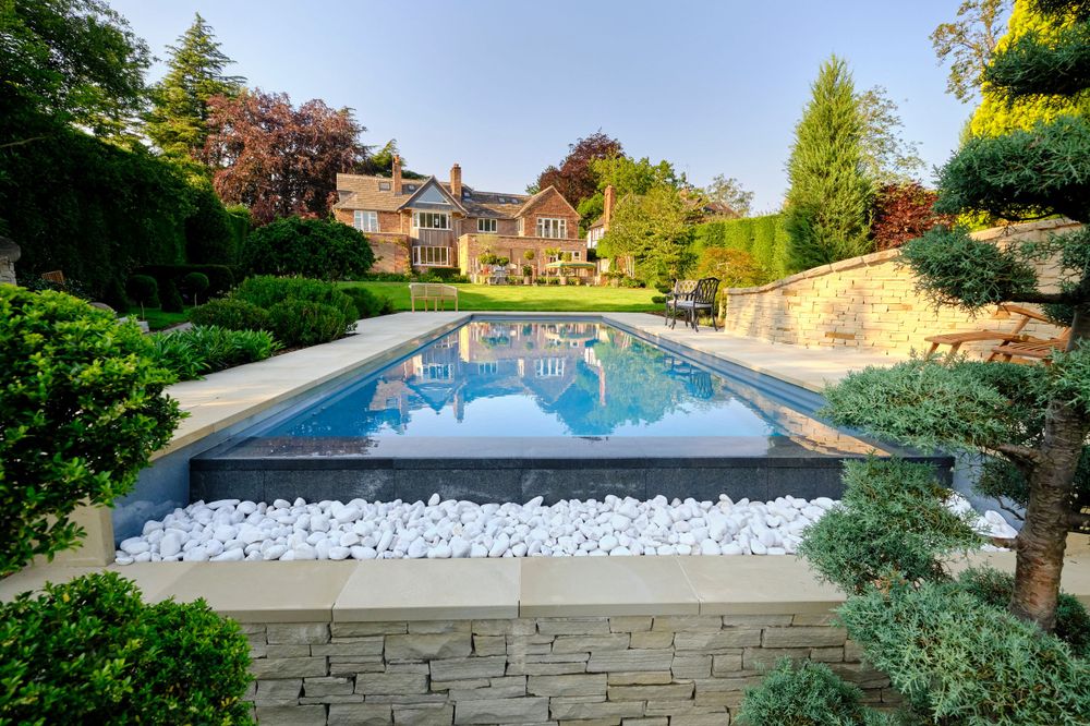 Luxury infinity pool with white stone border and landscaped garden at elegant country house.